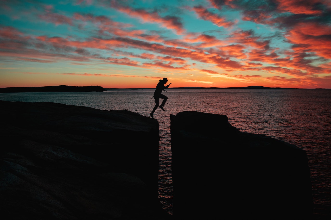 Silhouette of man leaping over cliff gap