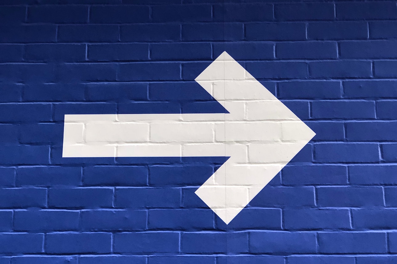 White arrow painted on blue brick wall