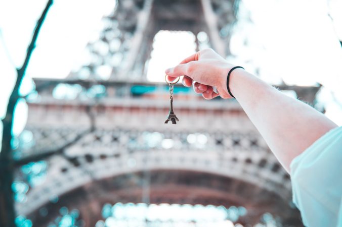 Girl holding Eiffel keychain in front of real Eiffel tower