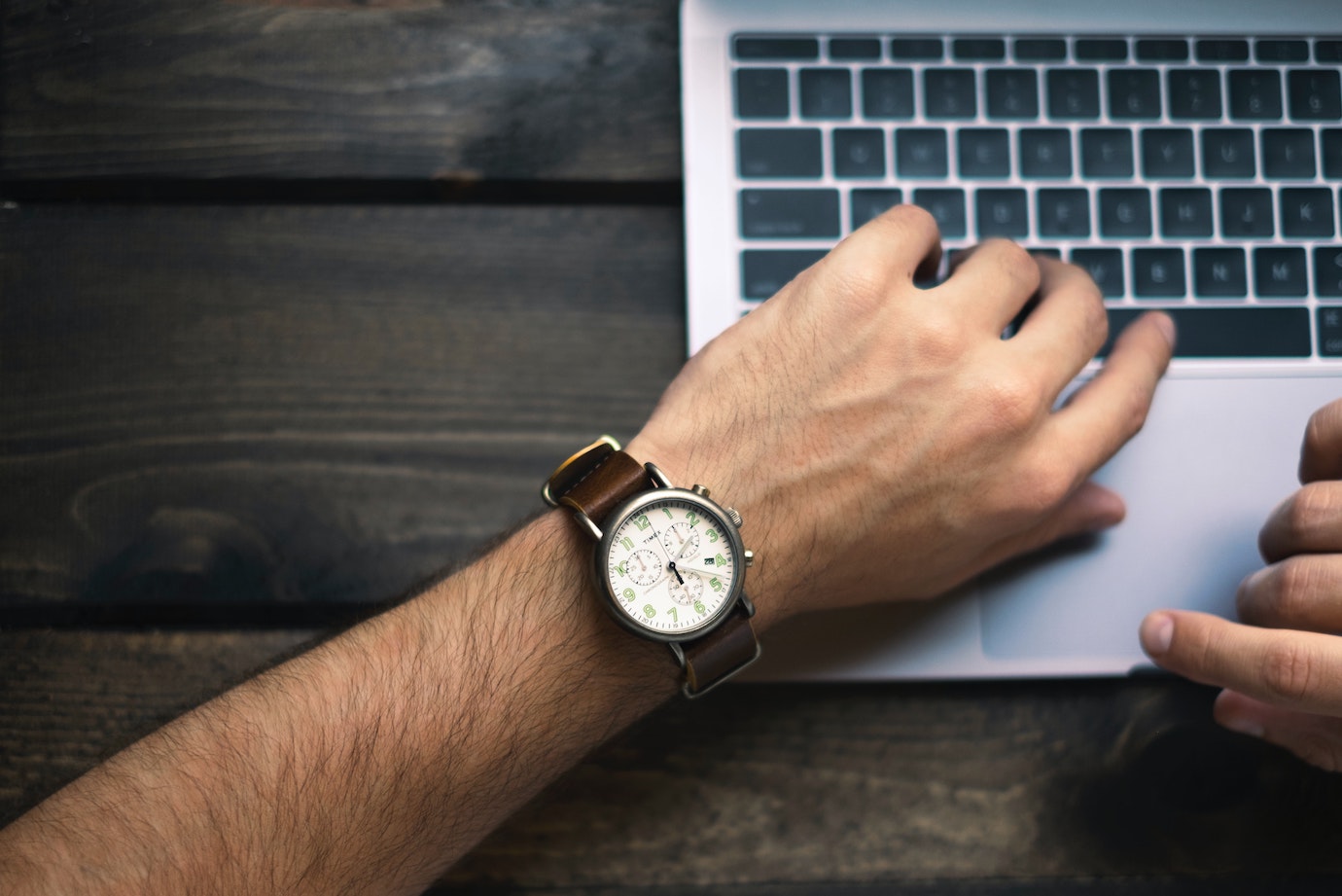 Man looking at Timex wristwatch with a laptop in the back