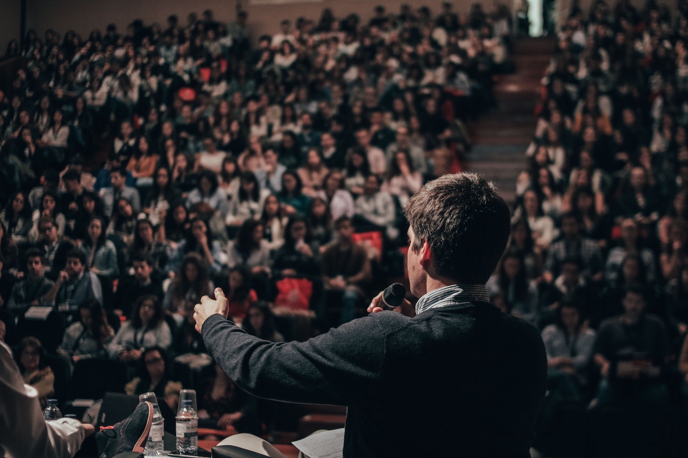 Man speaking on a stage to a crowd in a stadium