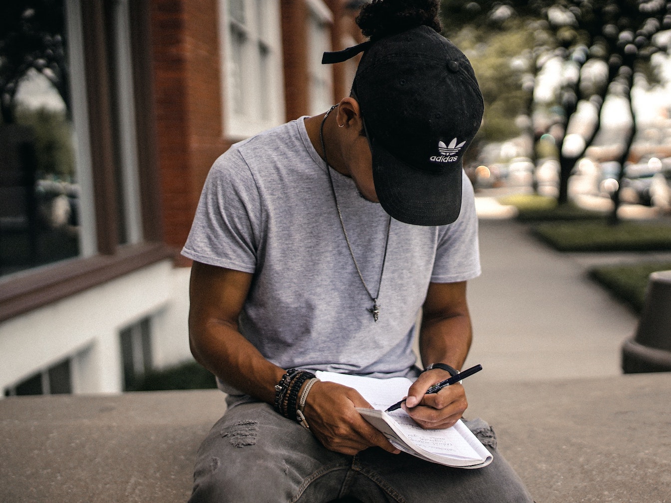 A man with a cap writing in a notebook