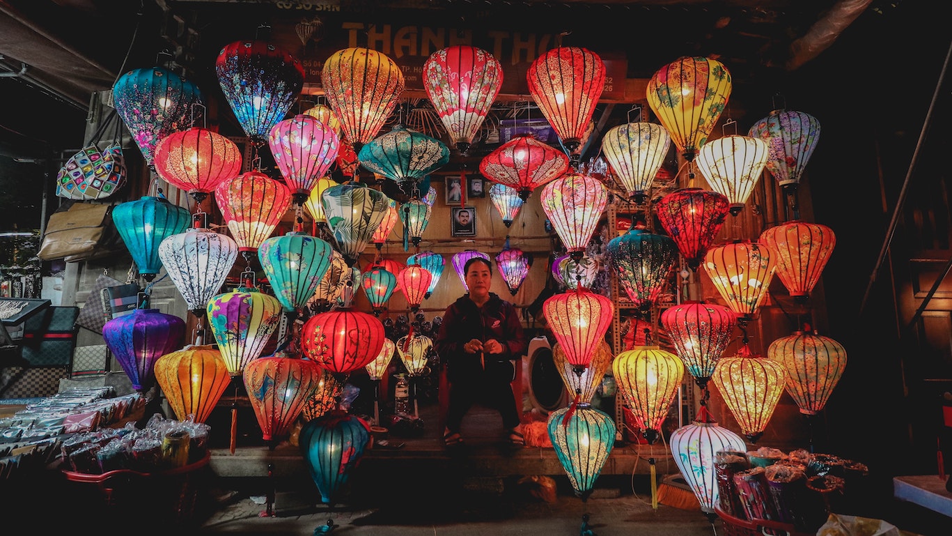 A woman standing below tens of colourful paper lanterns