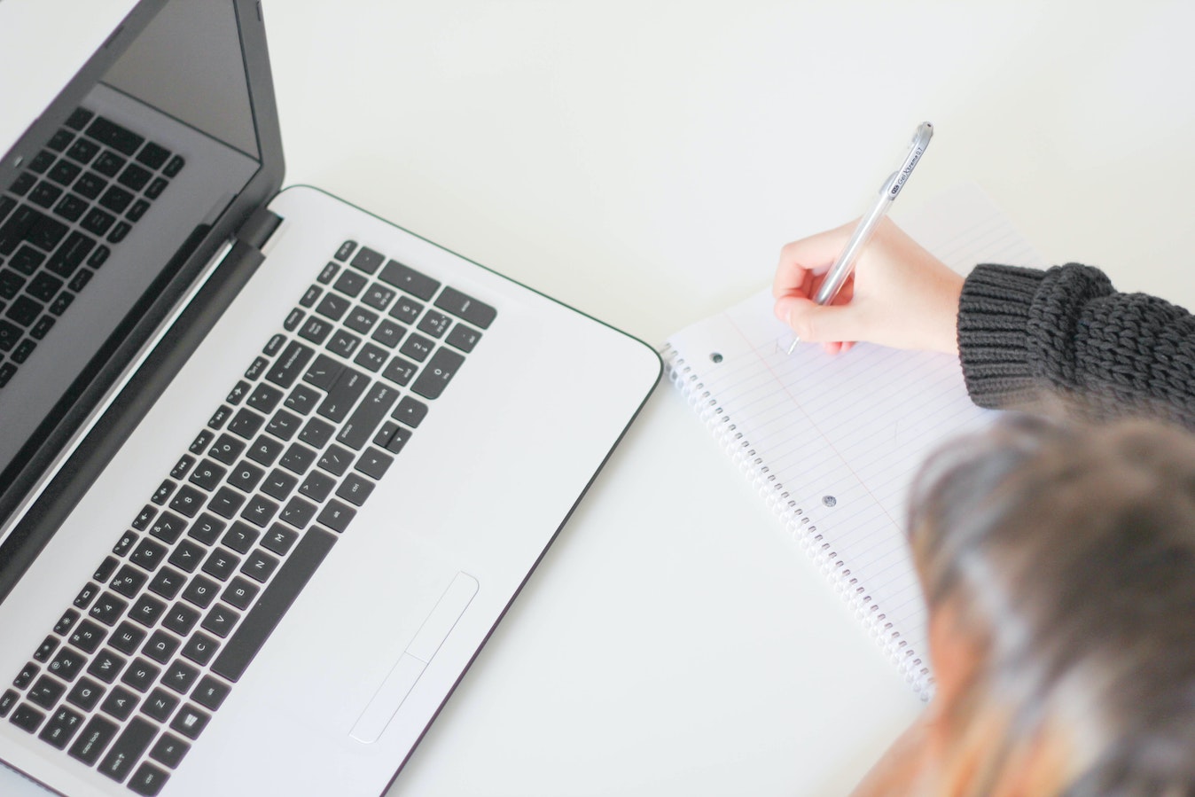 Woman writing on notepad in front of a laptop