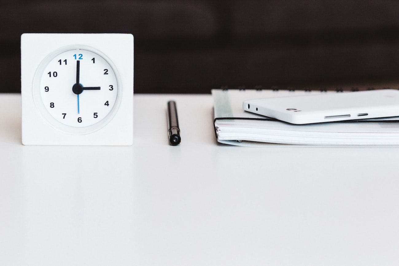 A clock, pen, notebook, and mobile phone, all in white