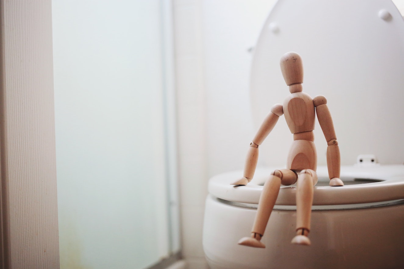 Wooden art mannequin sitting on a toilet