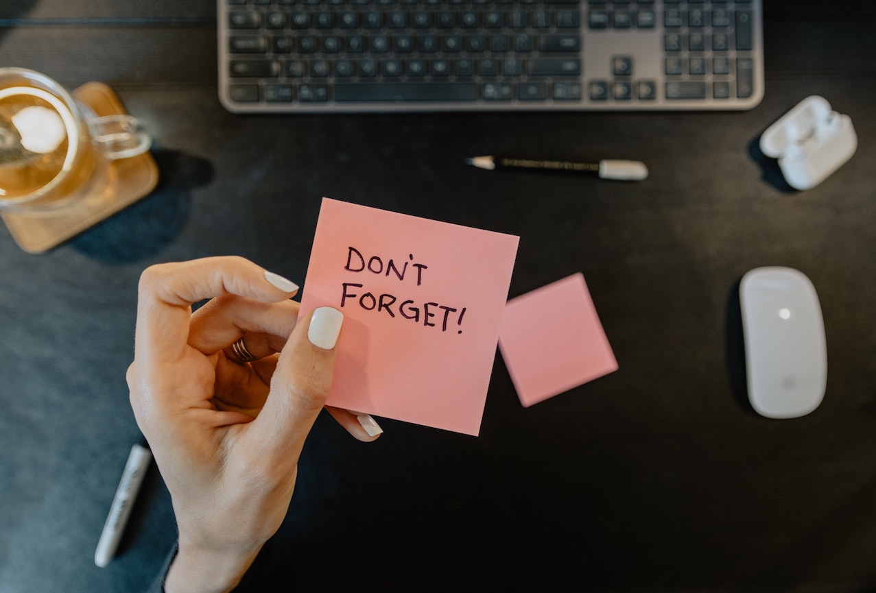 Post It note that says 'Don't Forget', on a desk with mouse and keyboard