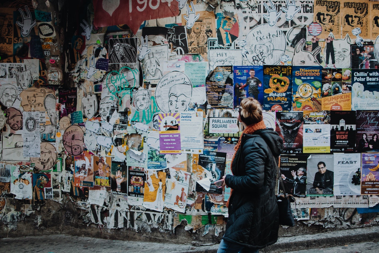 Blond woman in jacket looking at a wall full of posters