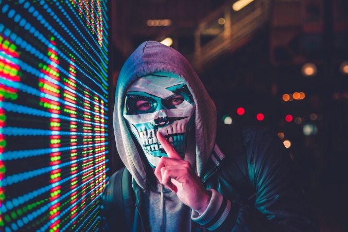 Man wearing mask and hoodie doing the shh sign
