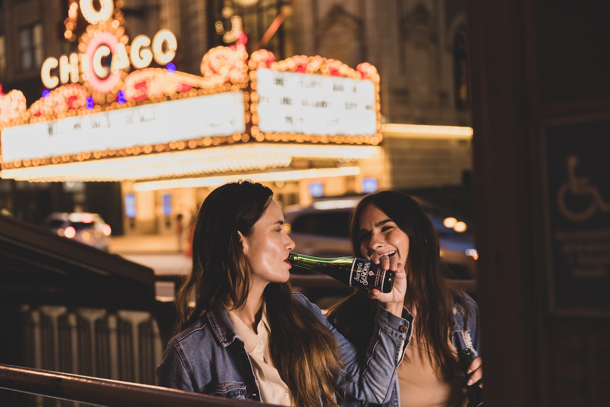 Two women sitting on bench drinking beers in front of theatre