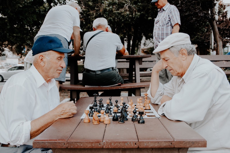 Two old men with caps playing chess on a park table